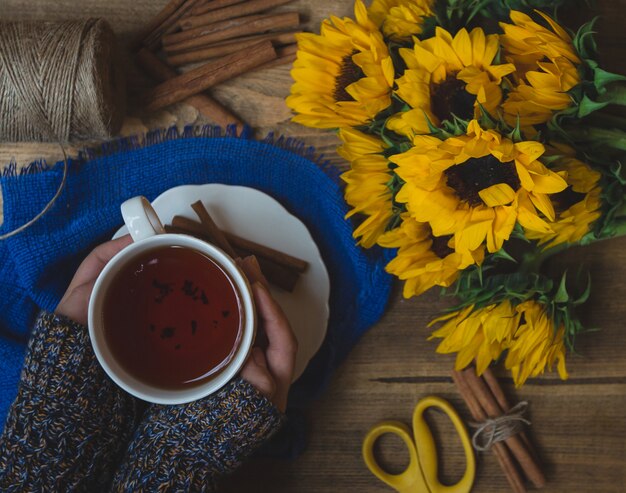 Girasoli e una tazza di tè caldo forata da una ragazza