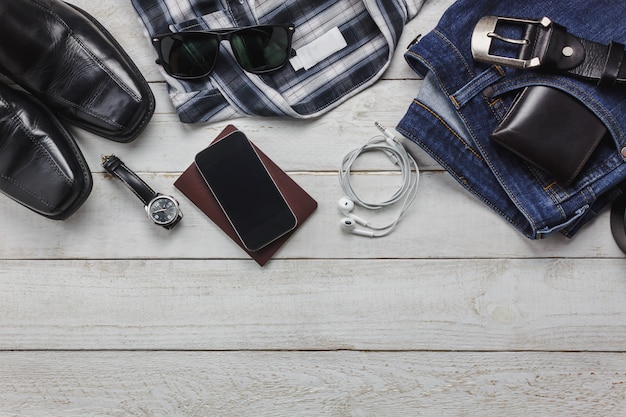 Gli accessi di vista superiore per viaggiare con il concetto di abbigliamento uomo. shirt, jean, telefono cellulare su background.watch di legno, occhiali da sole e scarpe sul tavolo di legno.