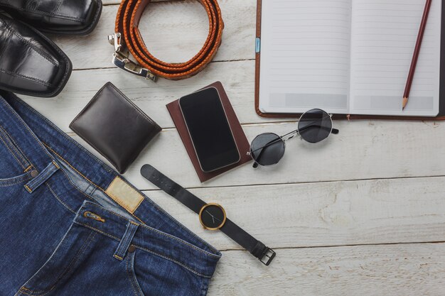 Gli accessi di vista superiore per viaggiare con il concetto di abbigliamento uomo. shirt, jean, telefono cellulare su background.watch di legno, occhiali da sole e scarpe sul tavolo di legno.