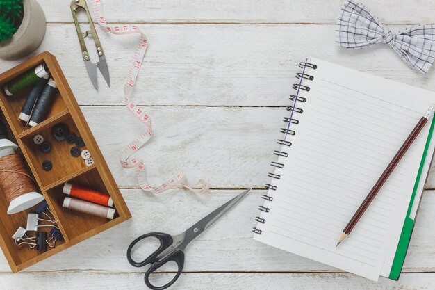 Gli accessori per il fissaggio sono di taglio forbici, cravatta di arco, bobine di filo, bottoni e abiti da cucire. Notebook per il testo spazio libero su sfondo rustico di legno.