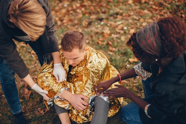 Gli amici aiutano il ragazzo. Il ragazzo ferito seduto per terra. Fornire il primo soccorso nel parco.