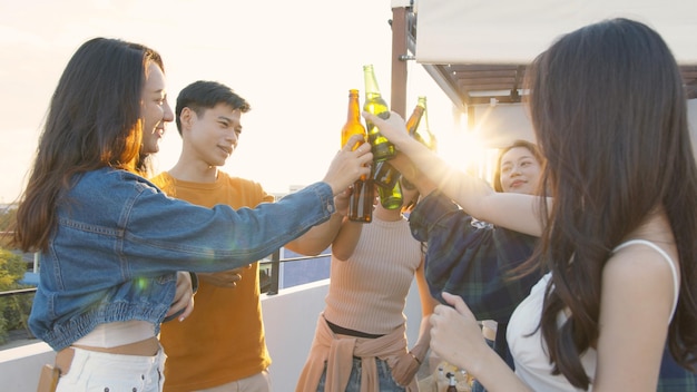 Gli asiatici che bevono alcolici al tramonto sul tetto fanno festa amici asiatici che tintinnano con bottiglie di birra