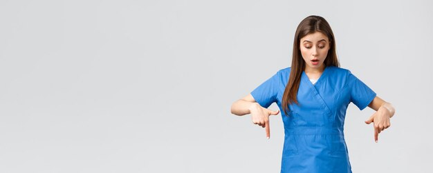 Gli operatori sanitari prevengono il virus covid19 test screening concetto di medicina Infermiera o dottoressa curiosa impressionata in camice blu che punta il dito verso il basso e guardando il banner si chiedeva