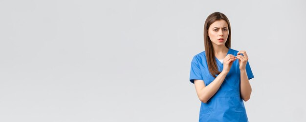 Gli operatori sanitari prevengono l'assicurazione contro i virus e il concetto di medicina Una dottoressa o un'infermiera scettica o confusa in camice blu guarda le unghie e gira la telecamera con la testa turbata non riesce a capire