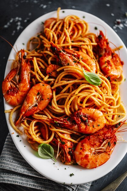 Gli spaghetti della pasta con i gamberetti e la salsa al pomodoro sono servito sul piatto su superficie scura. Avvicinamento.