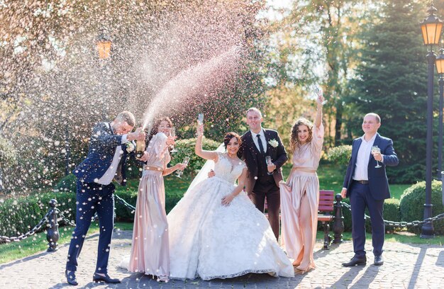 Gli sposi e i migliori amici bevono champagne e festeggiano nel parco il giorno del matrimonio