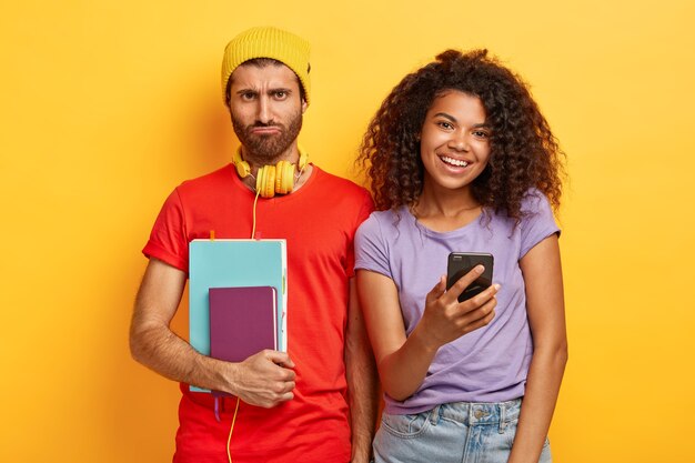 Gli studenti multietnici trascorrono insieme il tempo libero dopo le lezioni. La matricola stanca triste indossa cappello, maglietta rossa, tiene il diario e il taccuino