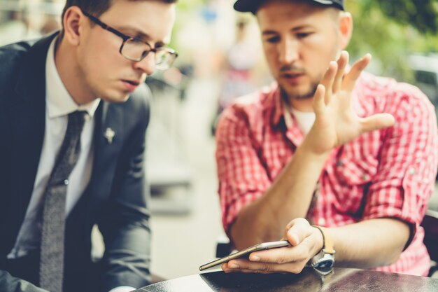 Gli uomini condividono notizie, foto, video sullo smartphone. Un uomo mostra ad un amico un&#39;applicazione in un telefono cellulare. Amici con uno smartphone, tecnologia.