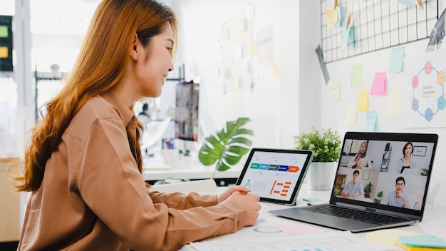 Gli uomini d'affari asiatici che usano il laptop parlano con i colleghi discutendo di brainstorming di affari sul piano nella riunione di videochiamata nel nuovo ufficio normale.