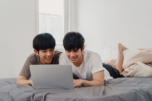 Gli uomini gay asiatici del lgbtq si accoppiano facendo uso del computer portatile del computer a casa moderna. Il giovane maschio dell'amante dell'Asia felice si rilassa insieme dopo il risveglio, guardando il film che si trova sul letto in camera da letto a casa di mattina.