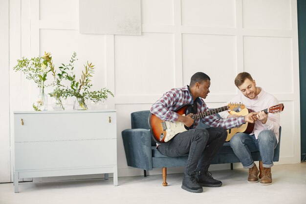 Gli uomini suonano la chitarra. Scrivere musica. Uomini africani e caucasici.