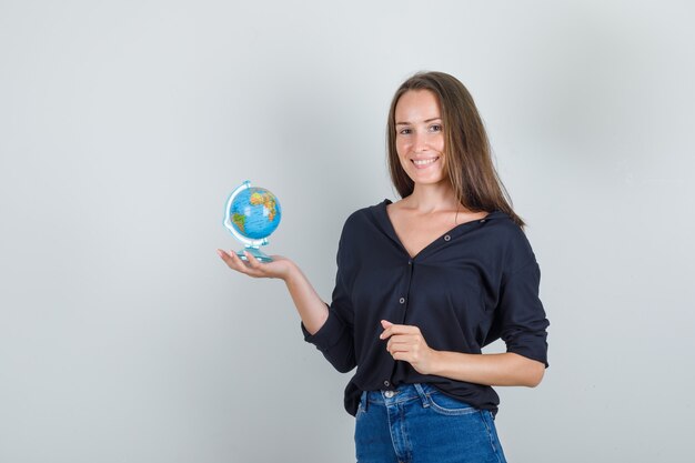 Globo della holding della giovane donna in camicia nera, pantaloncini di jeans e sguardo positivo