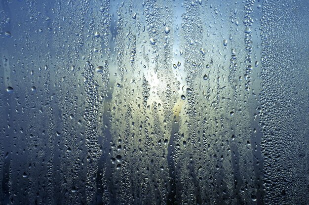 Gocce di pioggia d'acqua naturale su vetro sullo sfondo di struttura astratta della finestra