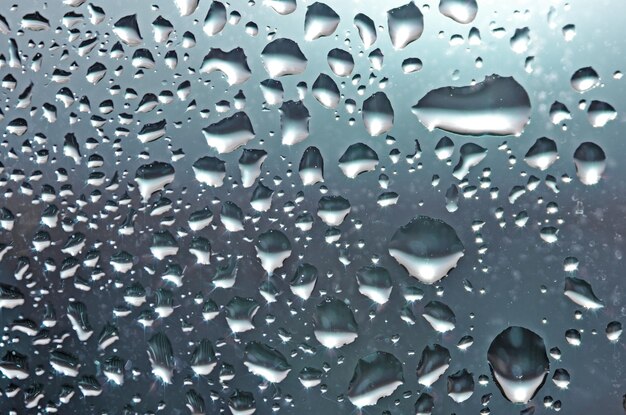 Gocce di pioggia d'acqua naturale su vetro sullo sfondo di struttura astratta della finestra