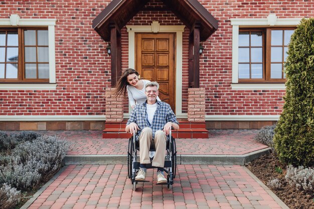 Godendo in famiglia uomo anziano in sedia a rotelle e figlia sorridente in giardino