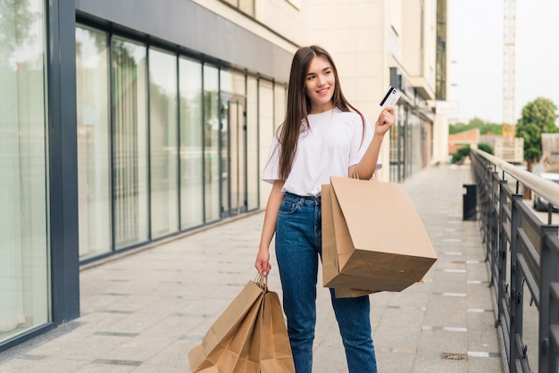 Godersi lo shopping di un giorno. Integrale della giovane donna che tiene i sacchetti della spesa e sorride mentre cammina lungo la strada