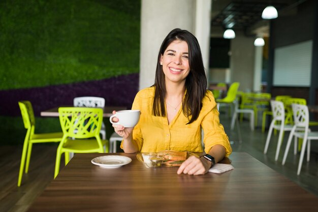 Godersi un momento di relax durante la pausa pranzo. Ritratto di una bella giovane donna che tiene una tazza di caffè e mangia un panino al food court