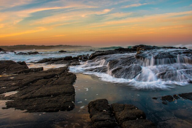 Grandangolo della spiaggia con formazioni rocciose durante il tramonto con un bel cielo