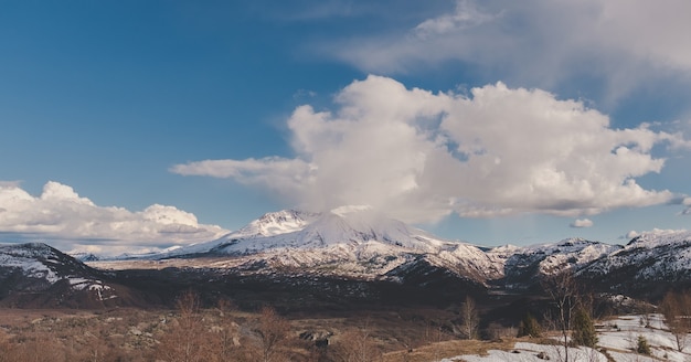 Grandangolo di montagne innevate in lontananza sotto un cielo nuvoloso blu