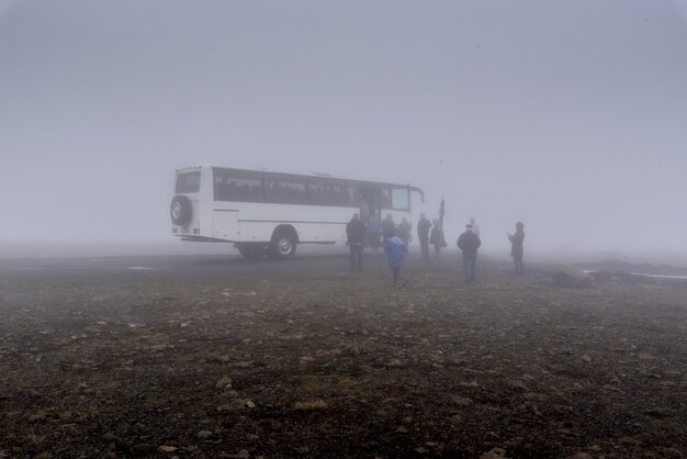 Grande autobus bianco e un gruppo di persone vicino ad esso in caso di nebbia in Islanda