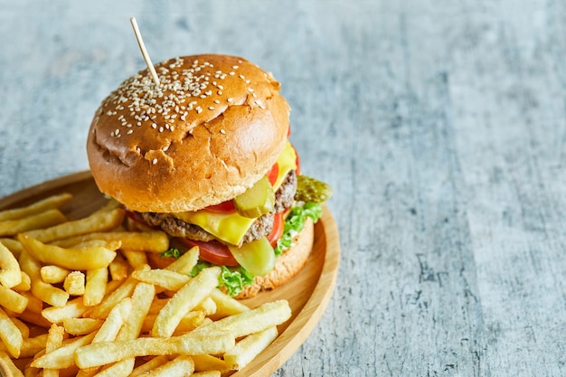 Grande hamburger con patate fritte nel piatto di legno sul tavolo di marmo.