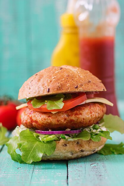 Grande panino - hamburger con hamburger di pollo succoso, formaggio, pomodoro e cipolla rossa sul tavolo di legno