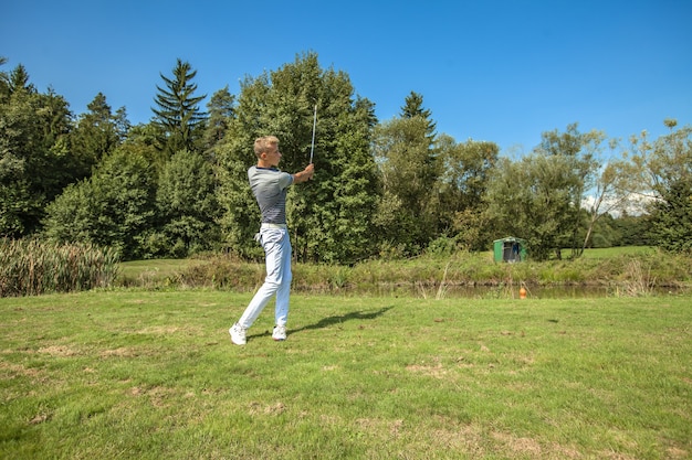 Grande scatto di un giovane che gioca a golf in un campo circondato da alberi in una giornata di sole