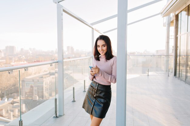 Grande vita di città, mattina di sole di giovane donna allegra sorridente sulla terrazza in attico con vista sulla città.