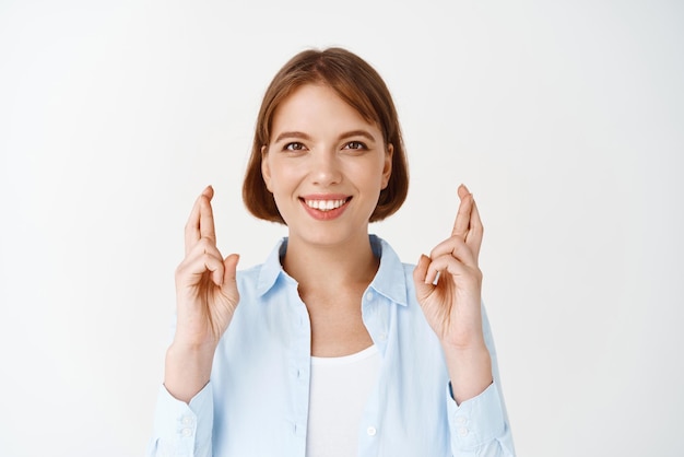 Grandi speranze Donna fortunata speranzosa incrociare le dita buona fortuna sorridendo e pregando in attesa di notizie in piedi su sfondo bianco