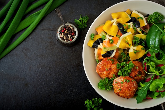 Grano duro di farfalle con polpette al forno di filetto di pollo in salsa di pomodoro e insalata in ciotola.