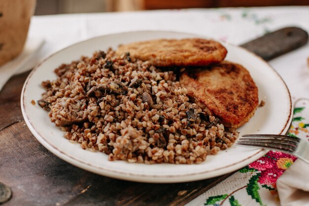 grano saraceno cotto insieme a fette di carne fritta all'interno di pagnotte di pane piatto bianco sul tavolo colorato di tessuti durante il giorno