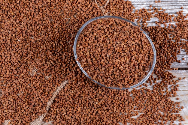 Grano saraceno in ciotola e accanto su bianco in legno. orizzontale, veduta dall'alto