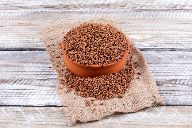 Grano saraceno in ciotola e intorno, su tela di sacco e legno bianco. orizzontale, veduta dall'alto