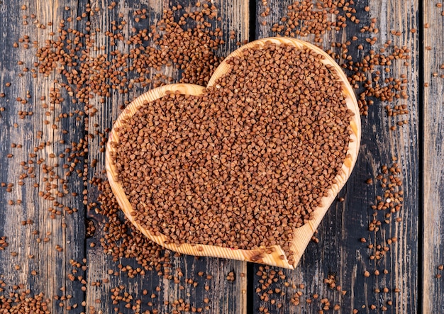 Grano saraceno in un tagliere a forma di cuore su un legno scuro. vista dall'alto.