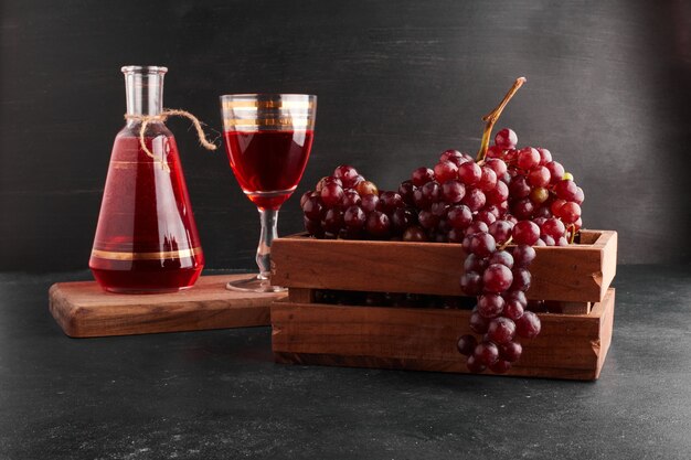 Grappoli d'uva rossa in un vassoio di legno con un bicchiere di vino sul nero.