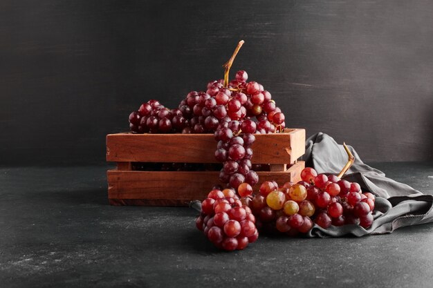 Grappoli d'uva rossa in un vassoio di legno sulla superficie nera.