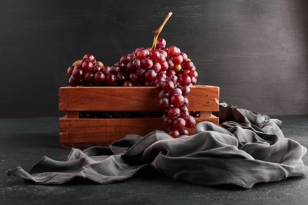 Grappoli di uva rossa in un vassoio di legno su sfondo nero.