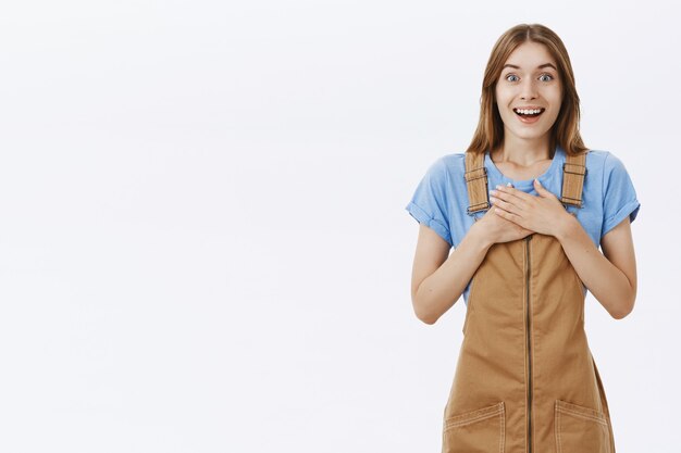 Grata ragazza giovane e carina, mano nella mano sul petto e sorridente, guardando sorpreso