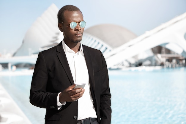 Grave fiducioso giovane imprenditore utilizza lo smartphone all'aperto in giornata di sole estivo