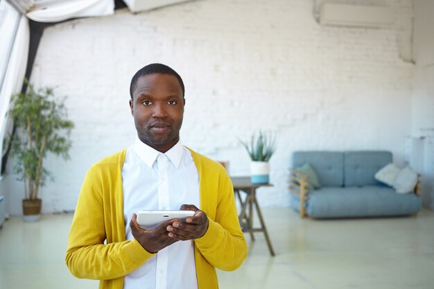 Grave fiducioso giovane uomo di razza mista in posa al chiuso, navigare in internet sul touchpad. Bel ragazzo africano utilizzando wifi sulla tavoletta digitale elettronica. Persone, stile di vita moderno, tecnologia e gadget