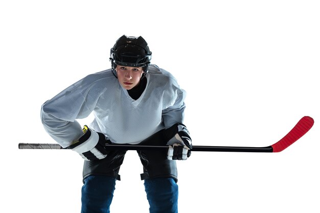 Grave. Giovane giocatore di hockey maschio con il bastone sul campo da ghiaccio e muro bianco. Sportivo che indossa attrezzature e pratica del casco. Concetto di sport, stile di vita sano, movimento, movimento, azione.