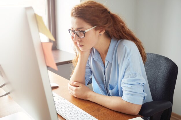 Grave impiegato femminile occupato, guardando lo schermo del computer, seduto in ufficio