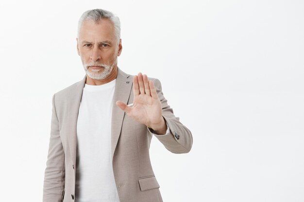 Grave imprenditore senior alzando la mano in gesto di arresto, disapprovare, vietare l'azione