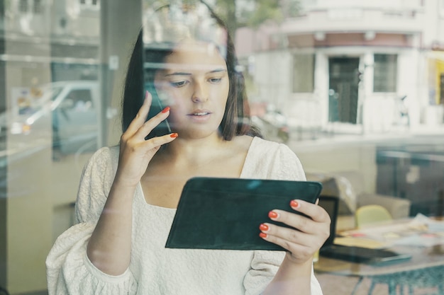 Grave imprenditrice parlando al cellulare, utilizzando tablet e guardando lo schermo