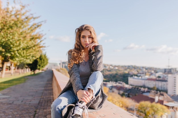 Grave ragazza ben vestita con i capelli ricci puntellando il viso con la mano