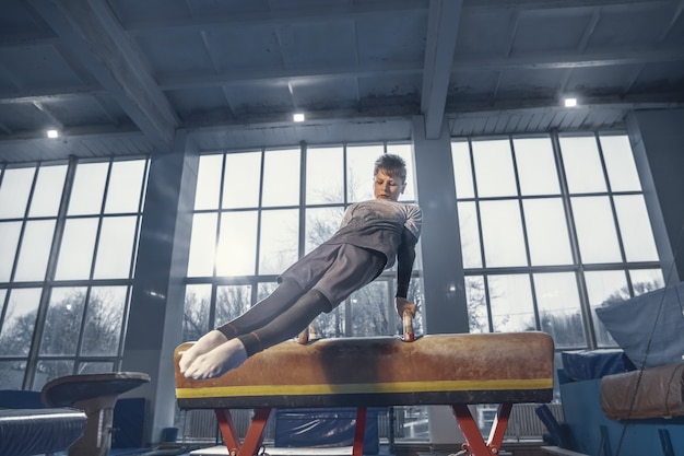 Grazia. Piccolo ginnasta maschio allenamento in palestra, flessibile e attivo. Ragazzino caucasico, atleta in abiti sportivi che praticano esercizi per la forza, l'equilibrio. Movimento, azione, movimento, concetto dinamico.