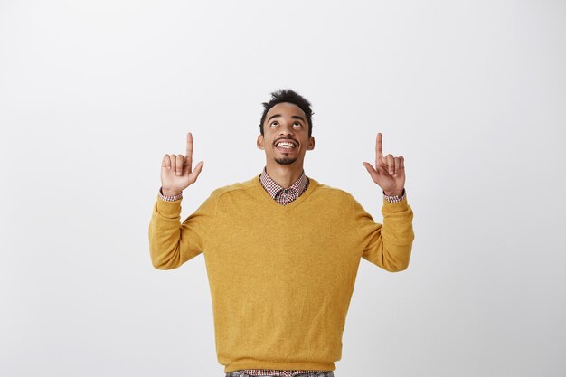 Grazie a Dio è venerdì. Ritratto di felice interessato giovane studente afro-americano in elegante maglione giallo alzando le mani, guardando e rivolto verso l'alto, godendo di una bella vista del cielo