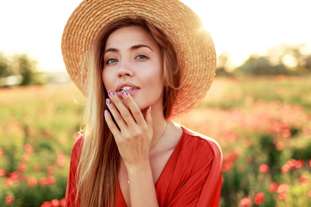 Graziosa donna dai capelli lunghi che guarda all'orizzonte, godendo della libertà. Ragazza seducente che propone nel campo del papavero. Calda luce del tramonto.