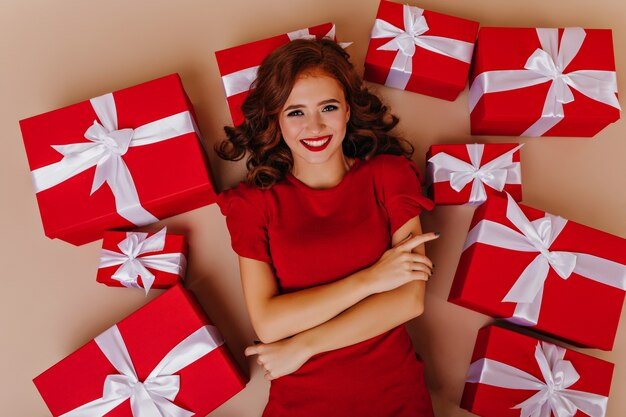Graziosa donna riccia di buon umore in posa sul pavimento con doni. Modello femminile attraente che gode della festa di Natale.