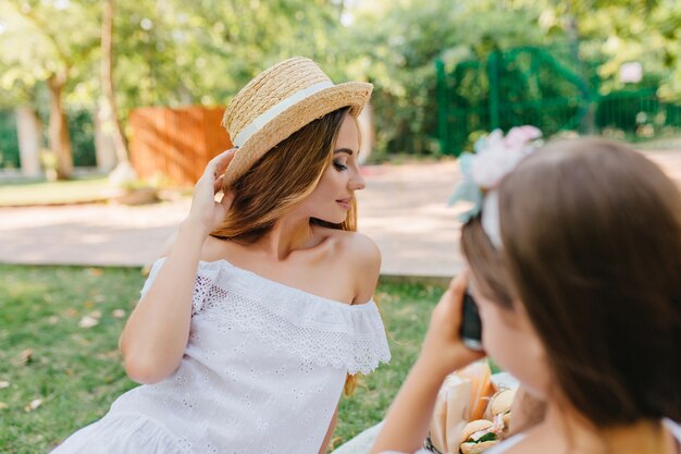 Graziosa giovane donna in elegante abito vintage in posa con gli occhi chiusi davanti alla figlia. Ragazza con i capelli scuri che tiene la macchina fotografica e fa foto della madre